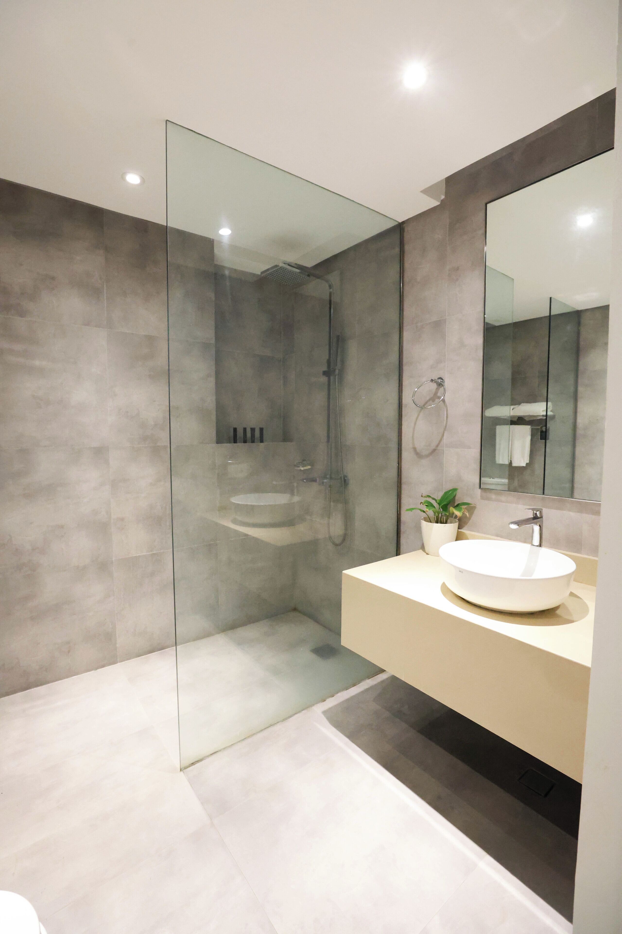 Un baño moderno con ducha de vidrio, lavabo redondo y un espejo grande.