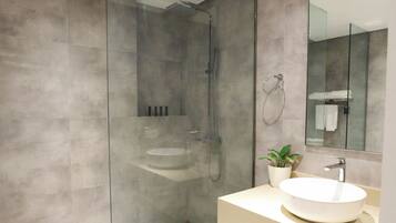 Un baño moderno con ducha de vidrio, lavabo redondo y un espejo grande.
