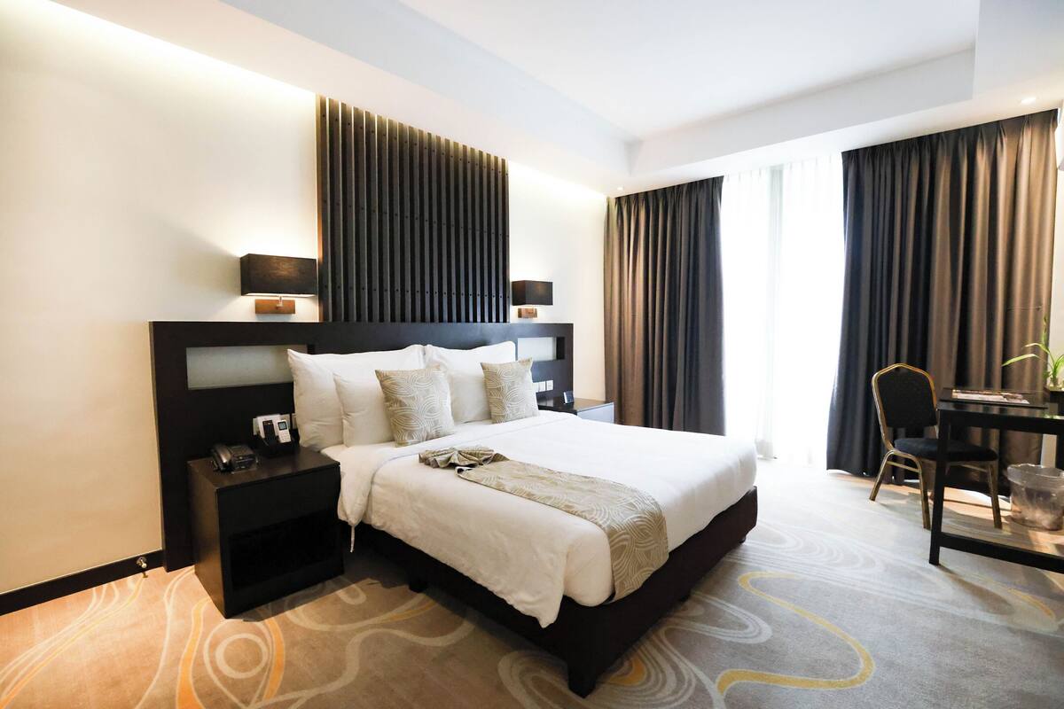 Una habitación de hotel moderna con una cama grande, mesitas de noche, un escritorio y una silla.