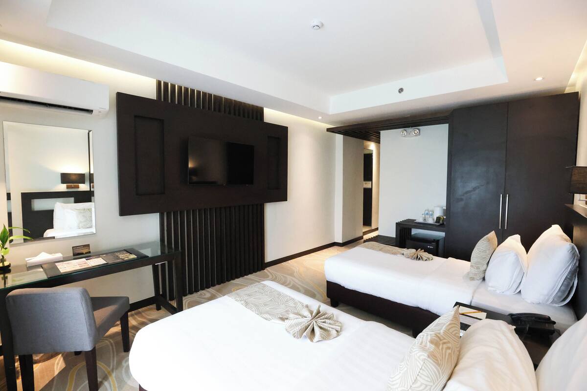 Una habitación de hotel moderna con una cama grande, un escritorio, un televisor montado en la pared y un armario.