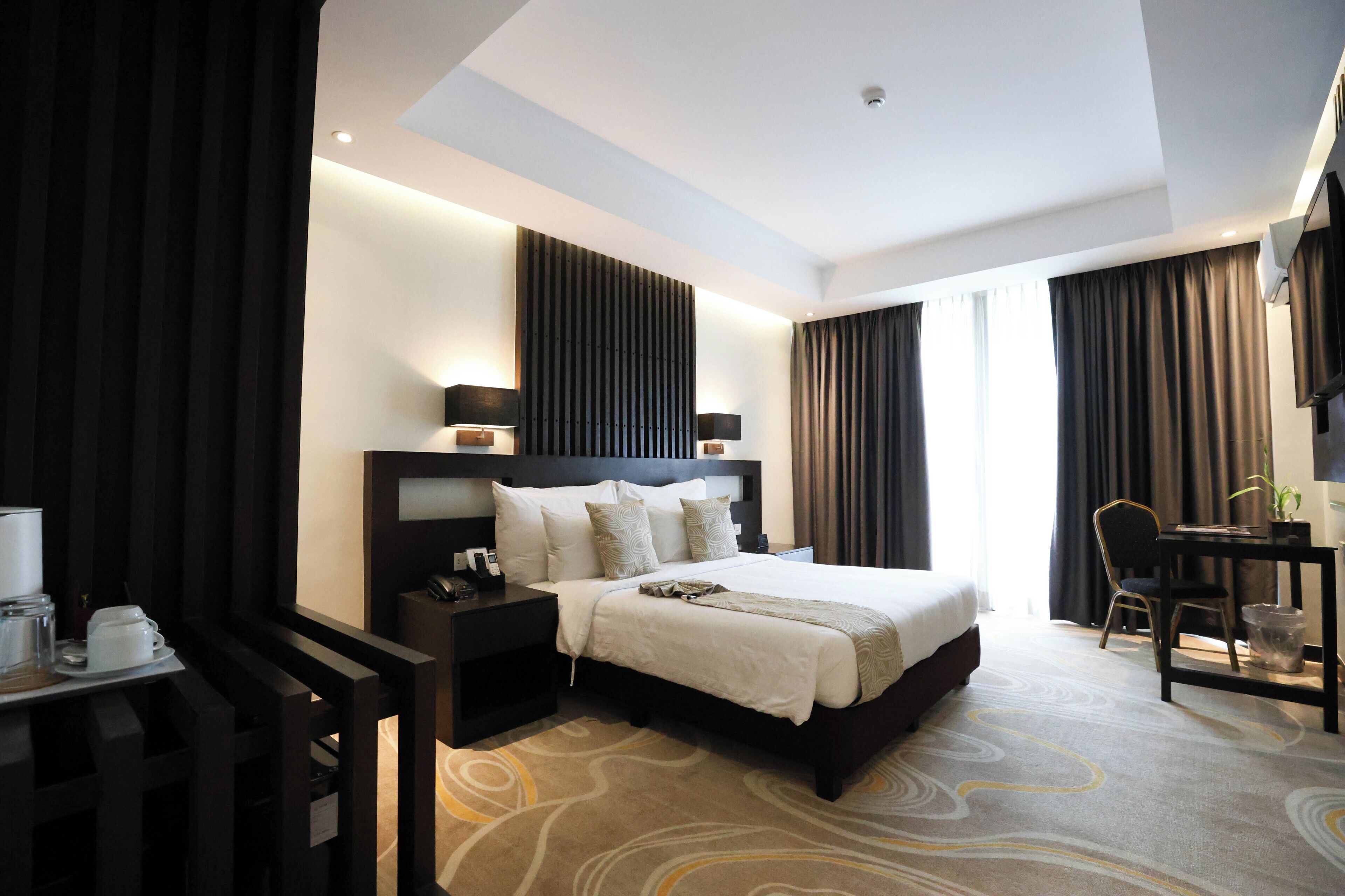 A modern hotel room with a large bed, bedside tables, a desk, and a chair.