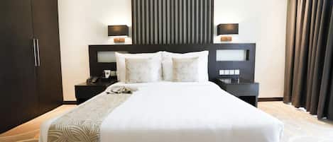 A modern hotel room with a large bed, dark wood headboard, bedside tables with lamps, and a large window with curtains.