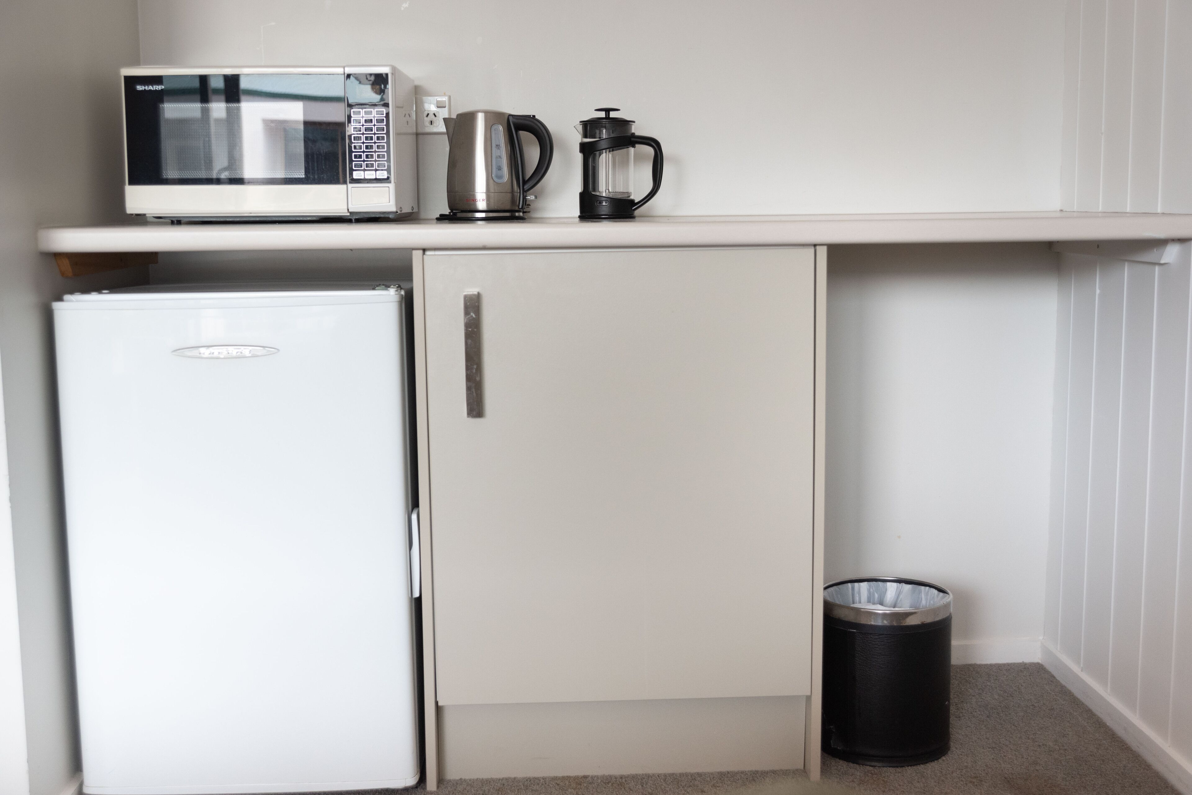 Una kitchenette compacta con microondas, cafetera y un refrigerador pequeño.