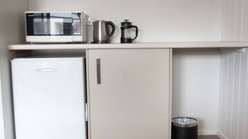 Una kitchenette compacta con microondas, cafetera y un refrigerador pequeño.