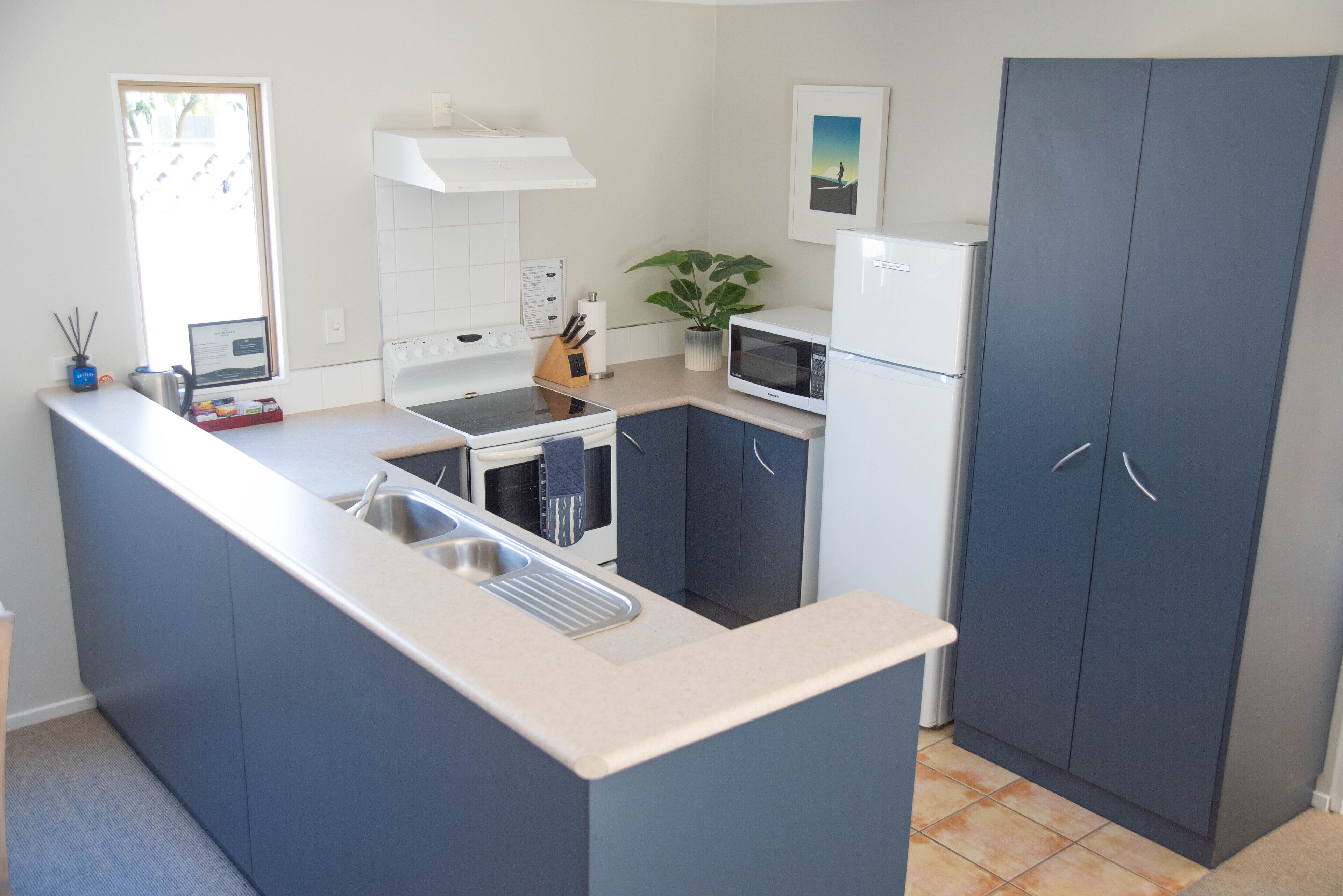 A compact kitchen with a central island, white appliances, and dark blue cabinetry.