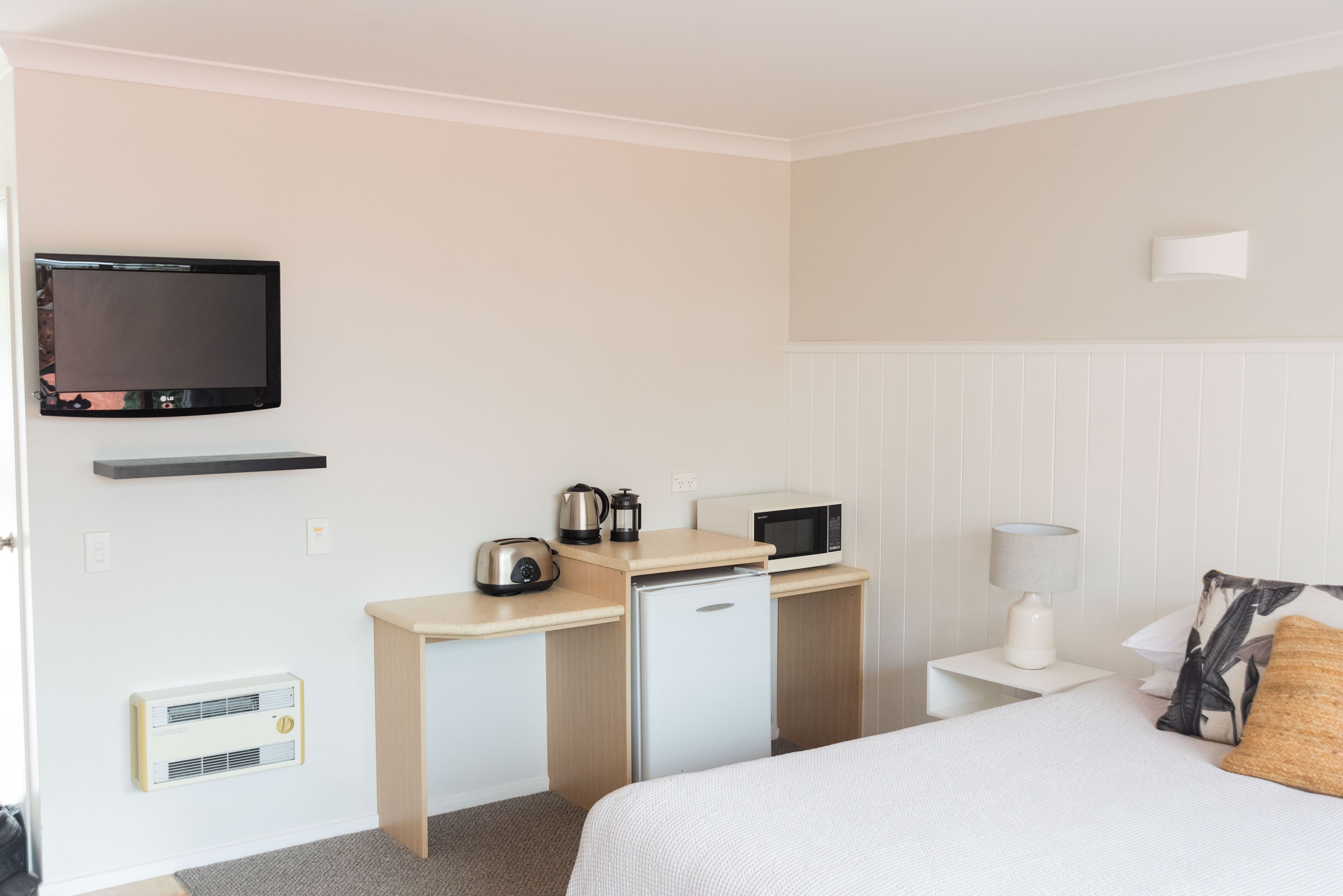 A hotel room with a bed, a desk with a microwave, a kettle, and a TV on the wall.