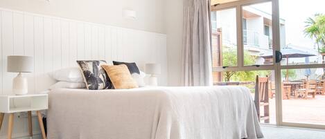 A bedroom with a large bed, white walls, and a sliding glass door leading to an outdoor area.