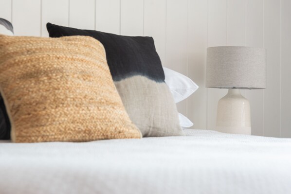 A neatly made bed with a white duvet, a beige and black pillow, and a white lamp on a bedside table. - Raglan Sunset Motel (Raglan)