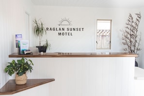 A reception desk at Raglan Sunset Motel with a wooden counter, a wall-mounted sign, and potted plants.