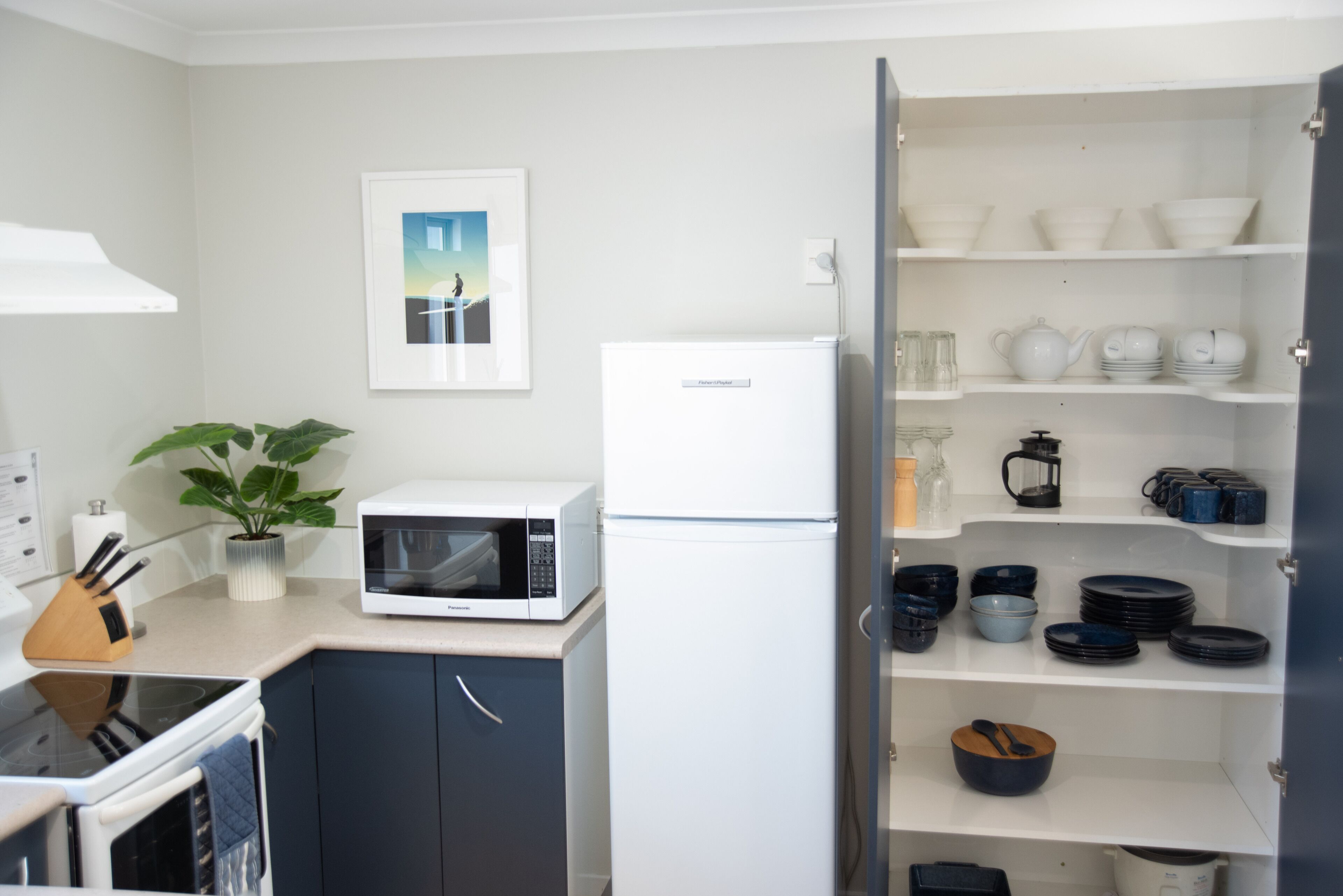 Cocina compacta con microondas, refrigerador y una variedad de platos y utensilios en estantes.