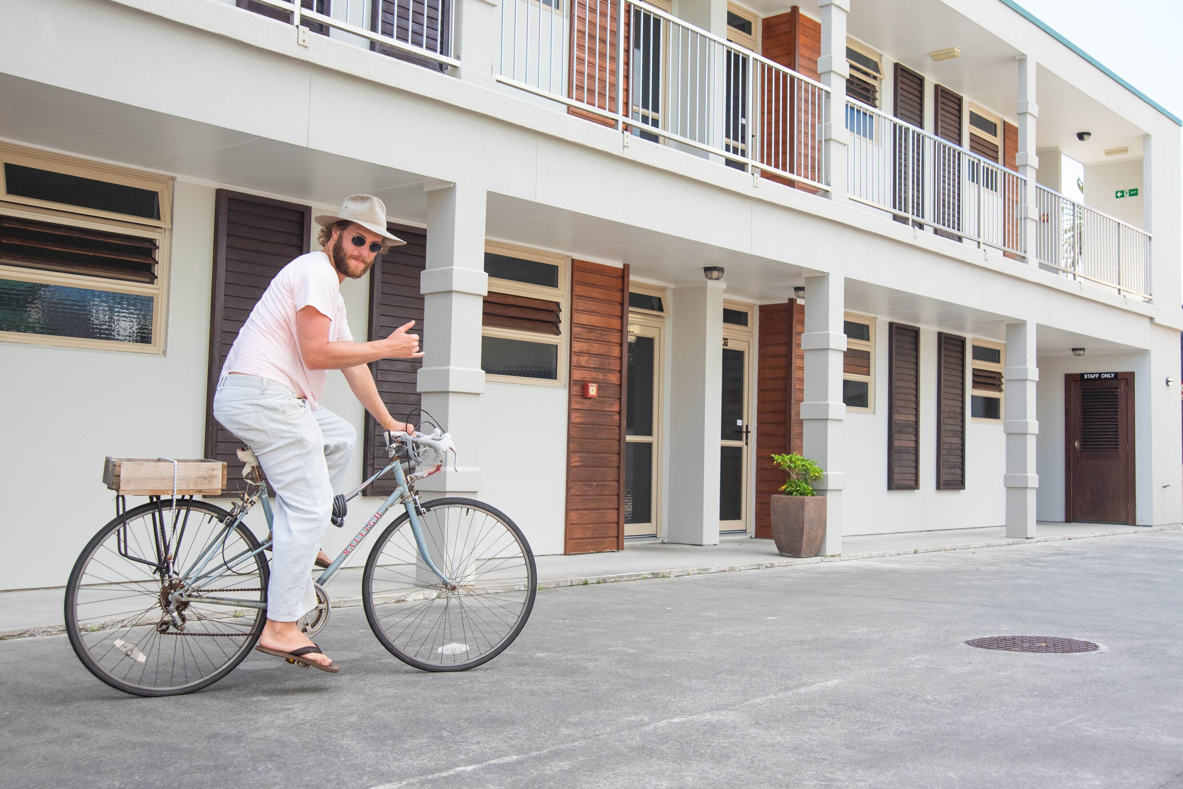Une personne à vélo se trouve devant un bâtiment doté d’un balcon, d’une porte en bois et d’une plante en pot.