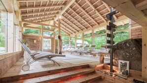 A wooden cabin with a sauna area featuring sun loungers and a stone fireplace. - Hotel Bad Schoergau (Sarentino)