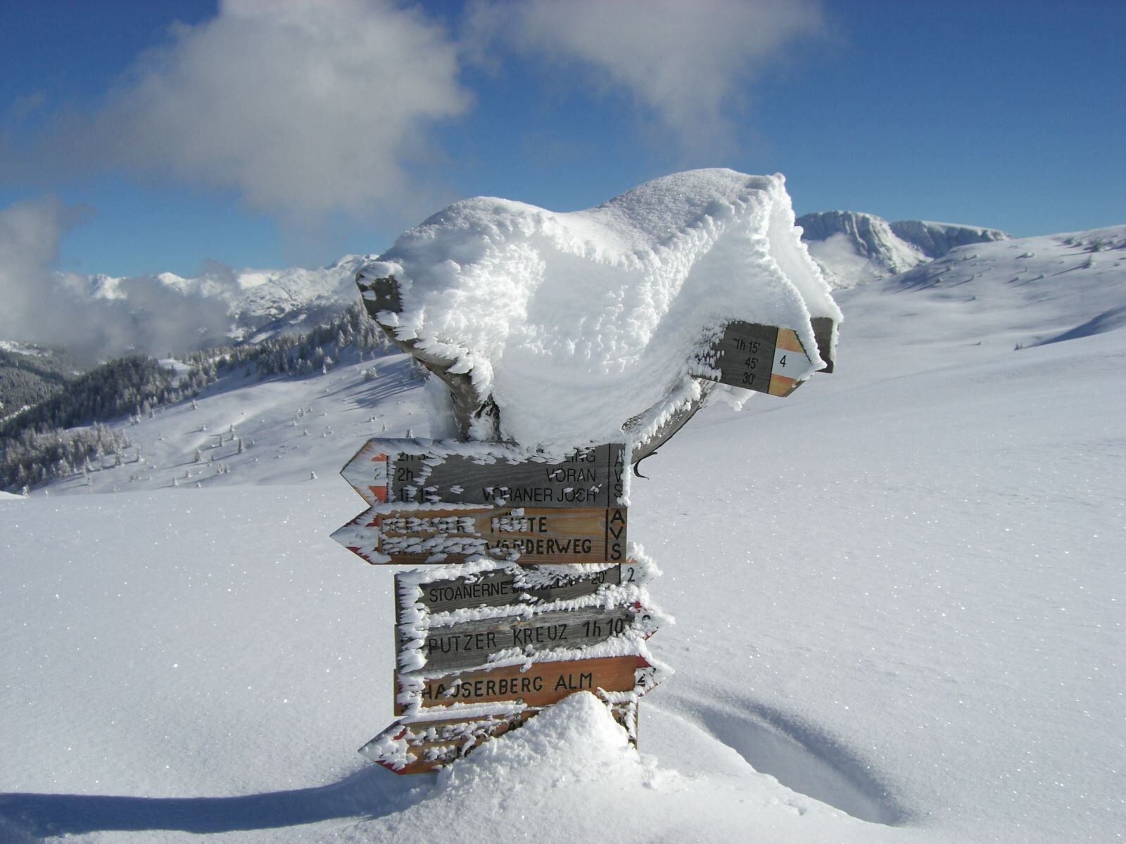 Un cartel indicador cubierto de nieve en una zona montañosa con varios destinos marcados.