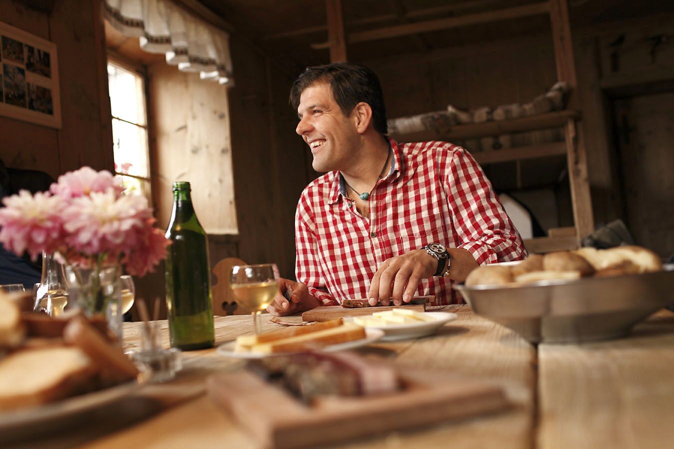 A wooden interior with a table set for a meal, including bread, a bottle, and a glass.