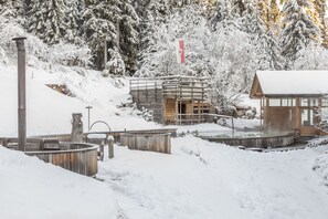 A wooden cabin with a metal roof, surrounded by snow-covered trees and a wooden deck. - Hotel Bad Schoergau (Sarentino)