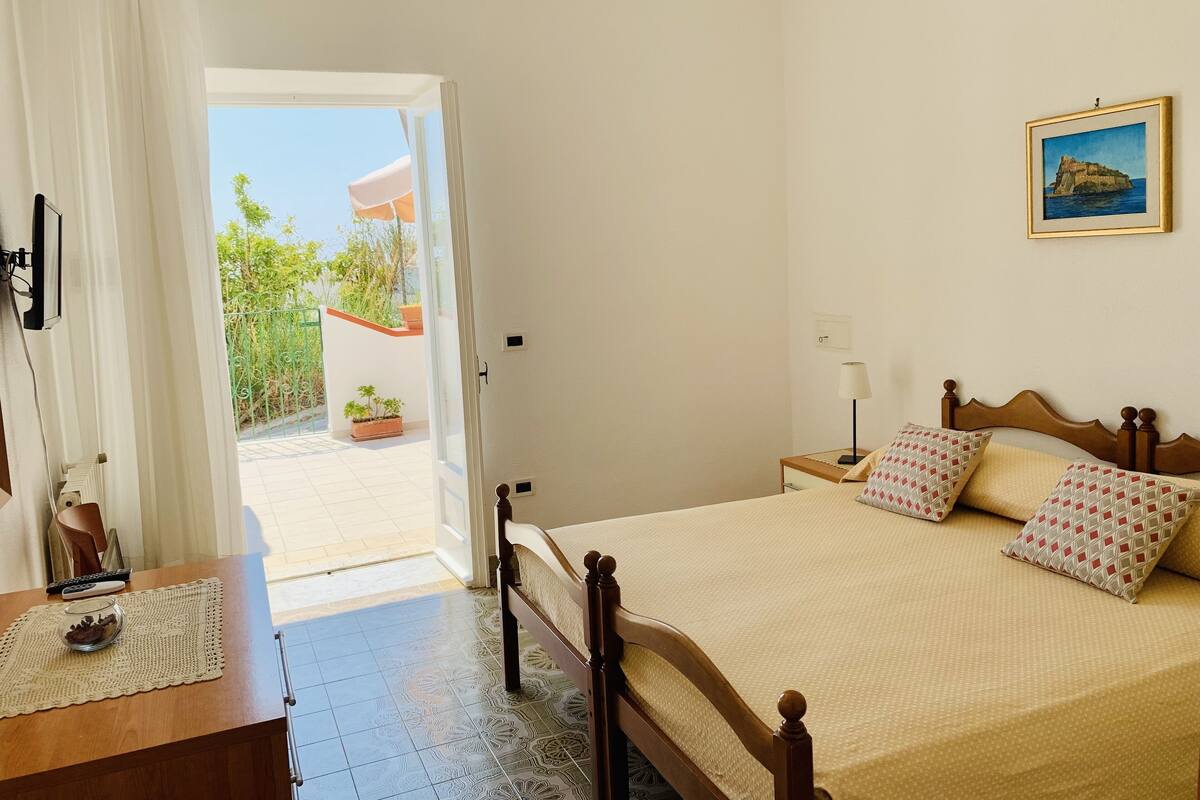 A bedroom with a bed, bedside table, and a view of the outside balcony.