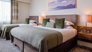Habitación de hotel con dos camas, cada una con ropa de cama verde, una mesita de noche con lámpara y un cuadro de un paisaje en la pared.