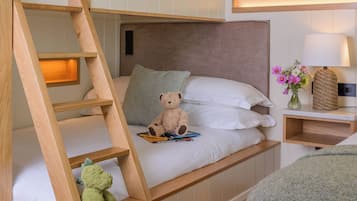 A bunk bed with a wooden ladder, a bedside table with a lamp, and a teddy bear on the lower bunk.