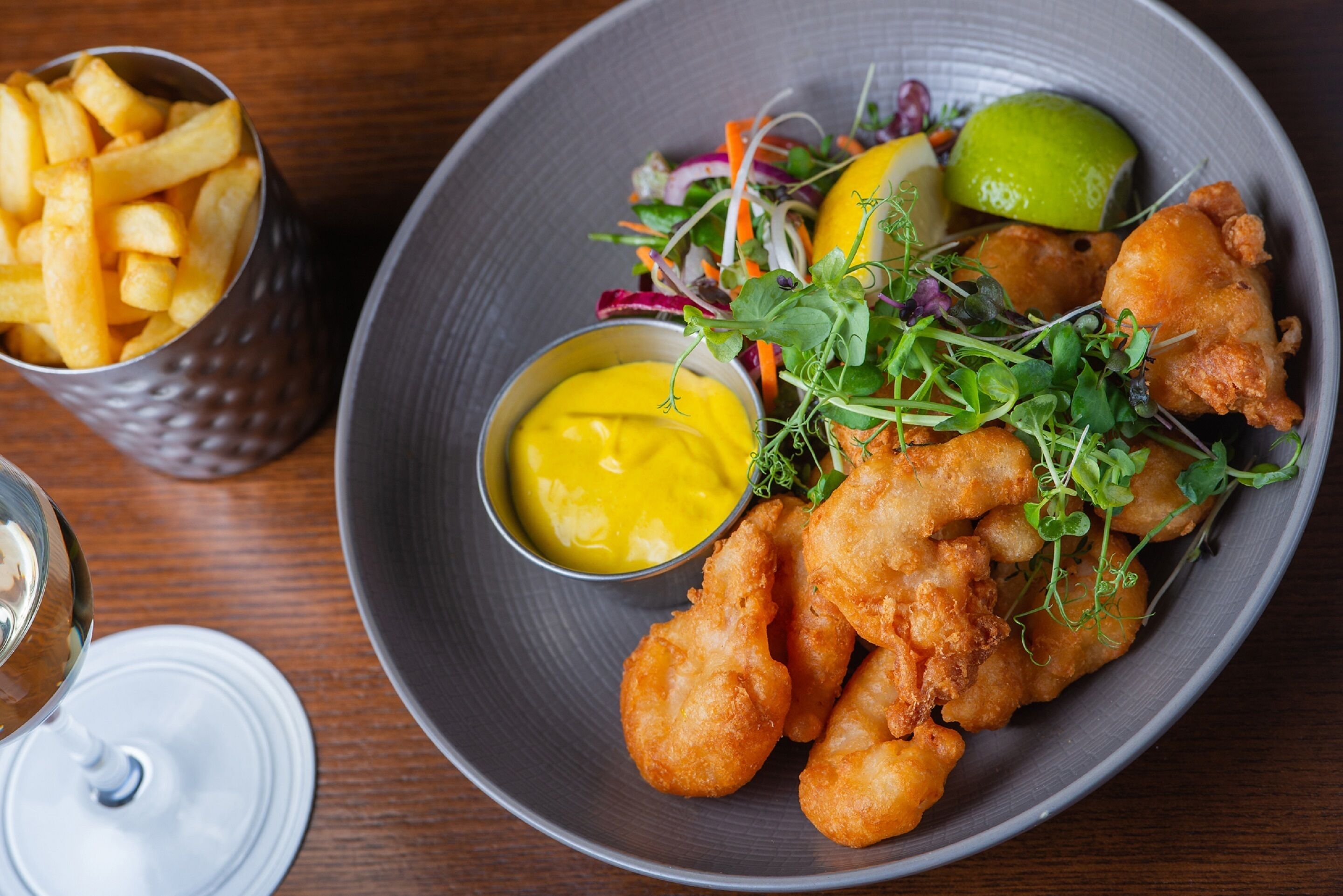 A plate of fried fish, fries, and salad with a side of mustard and a lime.