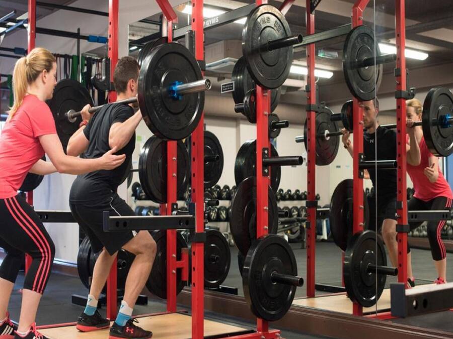 Uma academia com equipamentos de musculação e espelhos.