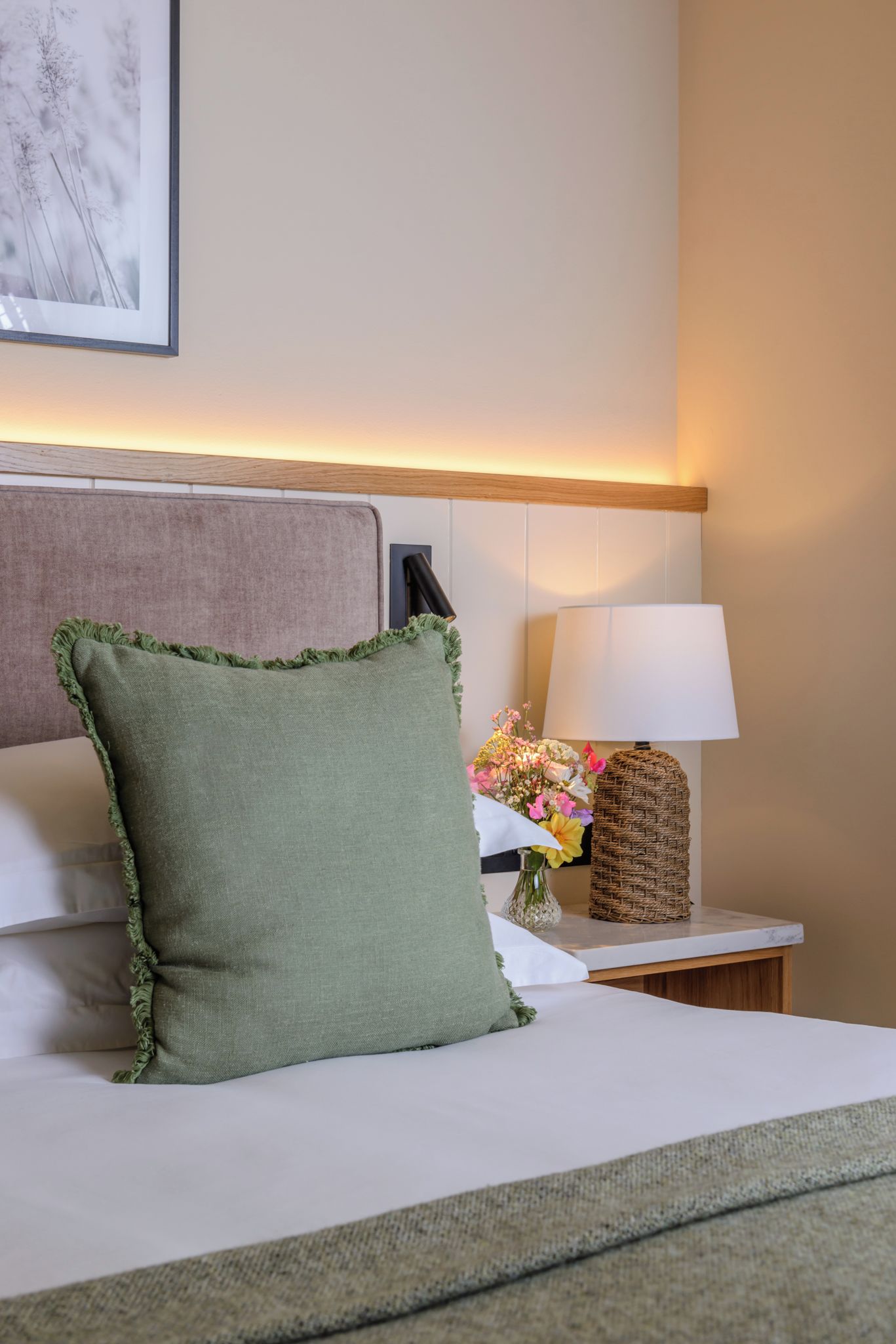 A hotel room with a bed, a nightstand with a lamp, and a vase of flowers.