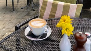 Café al aire libre con una mesa preparada para una bebida de café, un florero con flores amarillas y salero y pimentero.