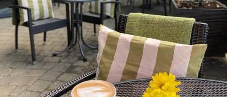 Café al aire libre con una mesa preparada para una bebida de café, un florero con flores amarillas y salero y pimentero.