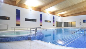Una piscina interior con paredes de azulejos, vigas de madera en el techo y una línea de agua clara.