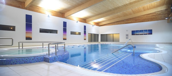 Una piscina interior con paredes de azulejos, vigas de madera en el techo y una línea de agua clara.
