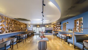 Un restaurante moderno con suelo de madera, asientos tapizados en azul y un área central de comedor con mesas y sillas.