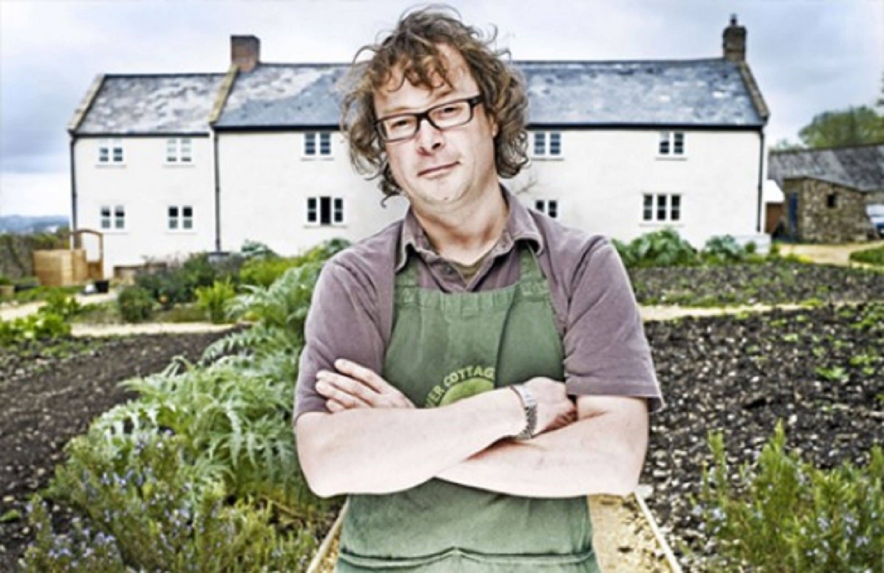 Une personne se tient devant un bâtiment blanc, avec un jardin en premier plan.