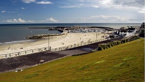 Una playa costera con un muelle, una playa arenosa y una colina cubierta de hierba.