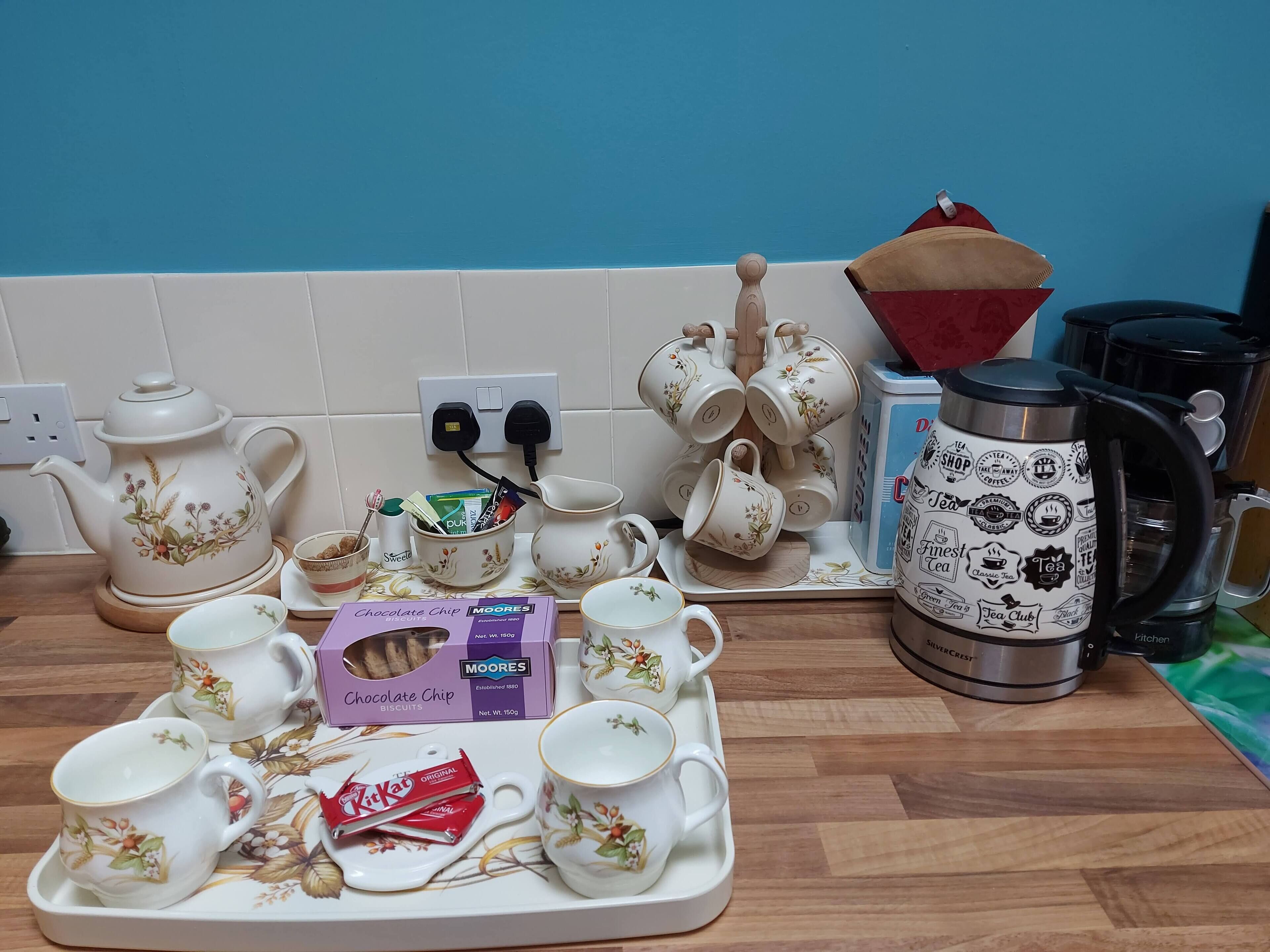 Un comptoir de cuisine avec tout le nécessaire pour préparer du thé, notamment une théière, des tasses, un plateau avec des biscuits et une boîte de biscuits aux pépites de chocolat.