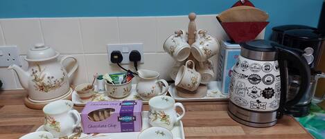 Un comptoir de cuisine avec tout le nécessaire pour préparer du thé, notamment une théière, des tasses, un plateau avec des biscuits et une boîte de biscuits aux pépites de chocolat.
