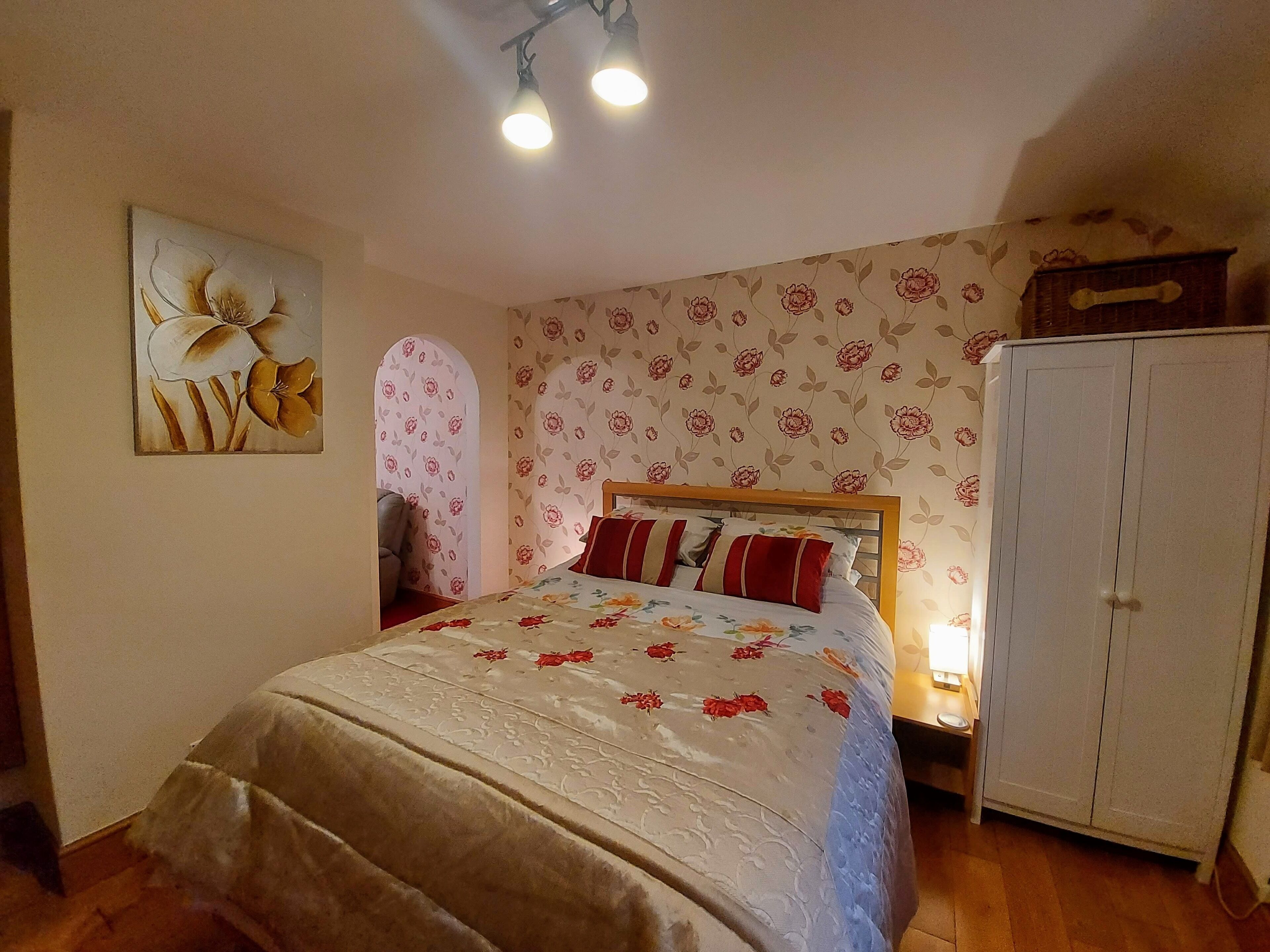 A bedroom with a bed, a wardrobe, and a floral wallpaper.