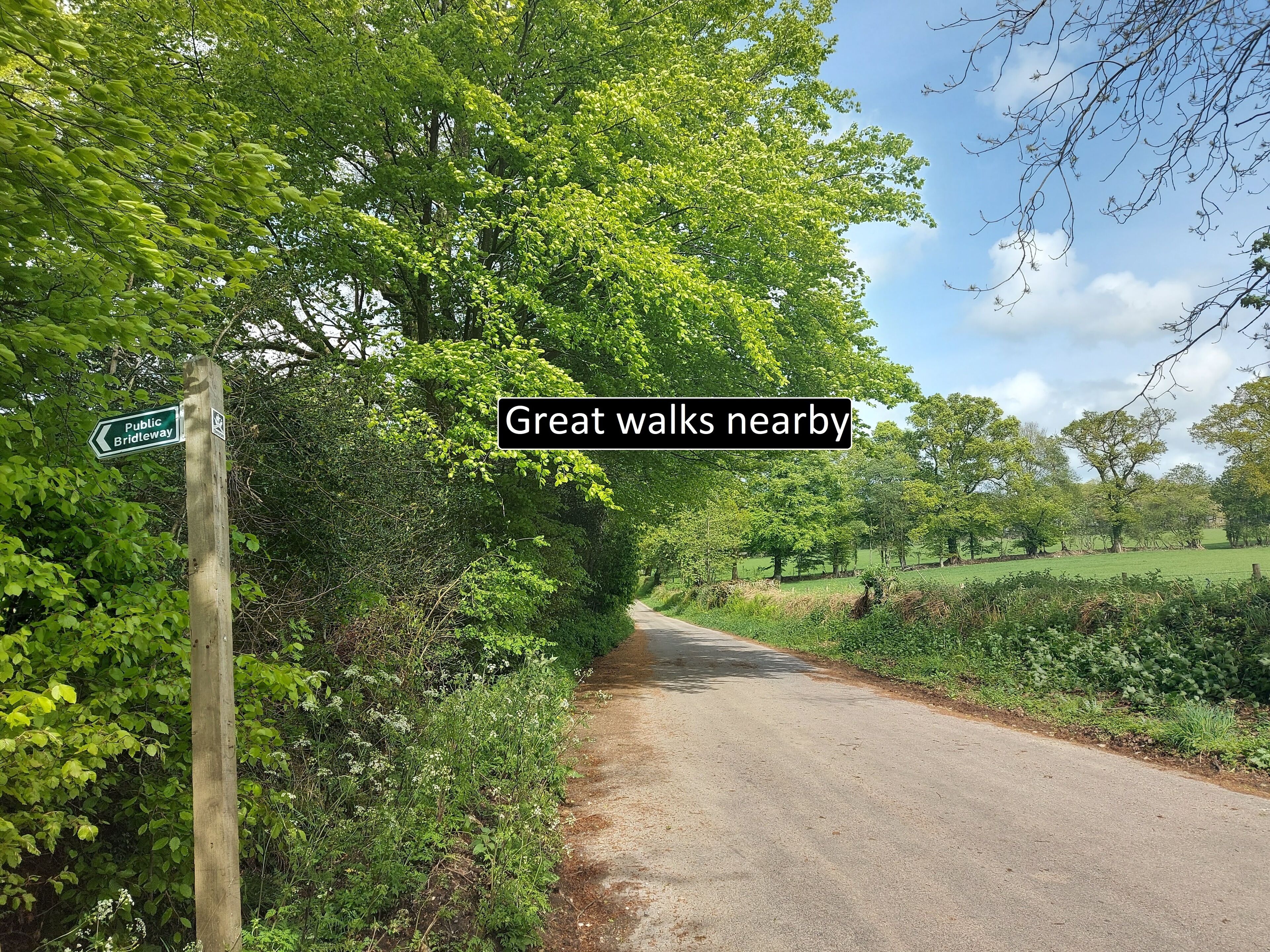 A rural road with a sign indicating a public bridleway and a text overlay suggesting nearby walks.