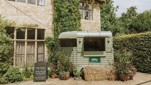 Un edificio rústico de piedra con una camioneta de comida verde con el rótulo “Milly’s” al frente.