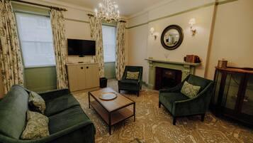 Una sala de estar con televisión, dos sillones verdes, una mesa de centro y una chimenea.