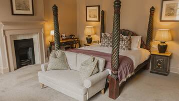 A four-poster bed with a headboard, a fireplace, a sofa, and two nightstands with lamps.