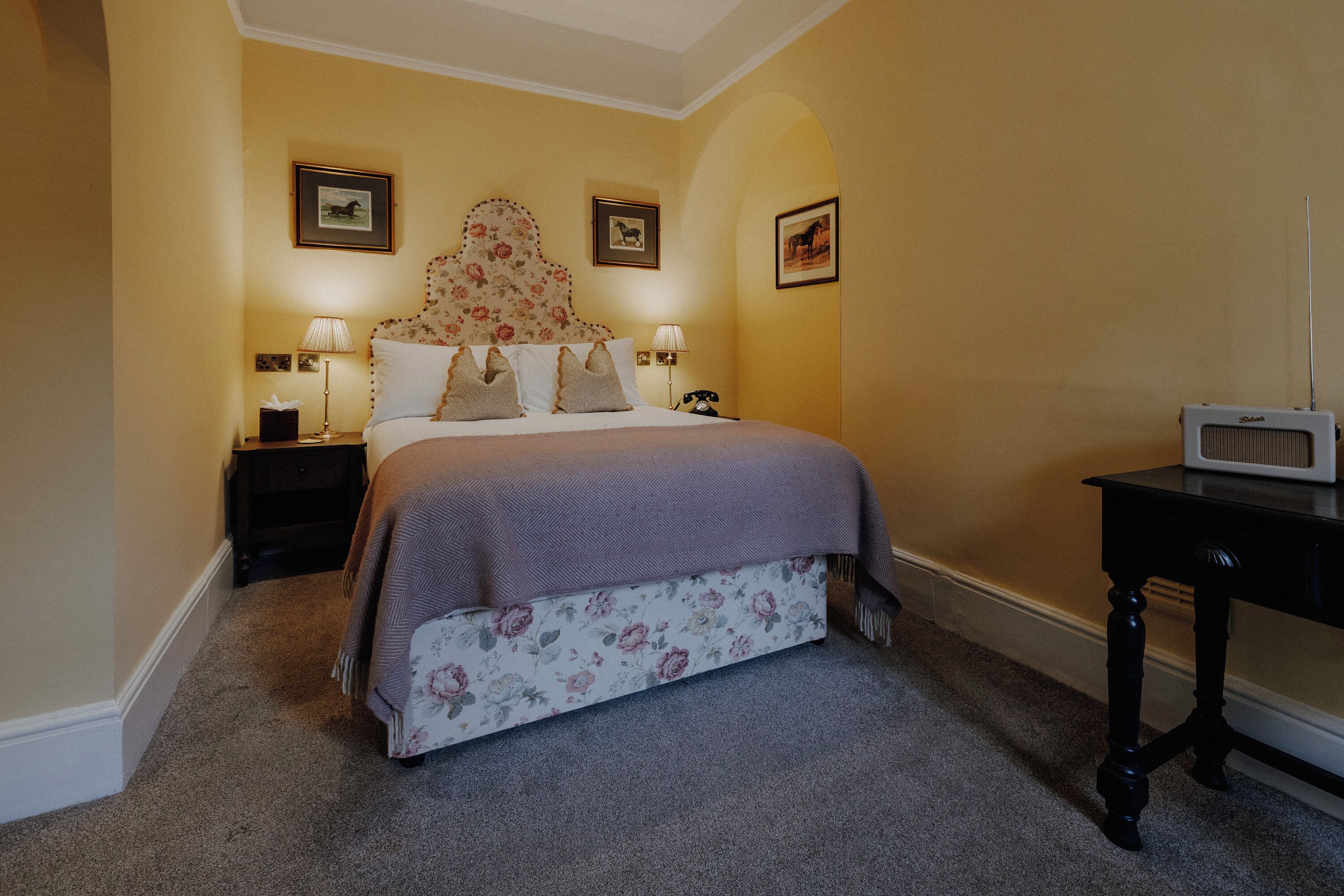 A bedroom with a floral bedspread, two bedside lamps, a nightstand, a bedside telephone, and a television on a stand.
