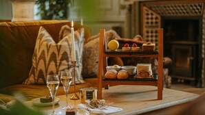 Un salón acogedor con una mesa de centro de madera que sostiene diversos pasteles y postres, una vela y copas de vino.