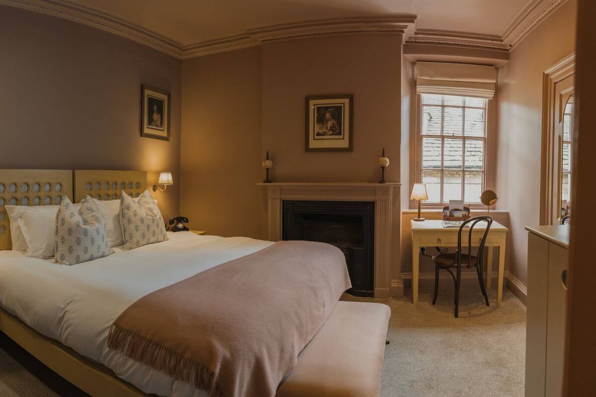 A bedroom with a large bed, bedside tables, a desk, and a fireplace.
