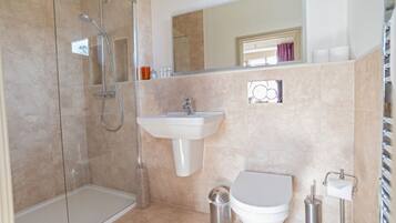Een moderne badkamer met een douchecabine van glas, een witte wastafel en een toilet.
