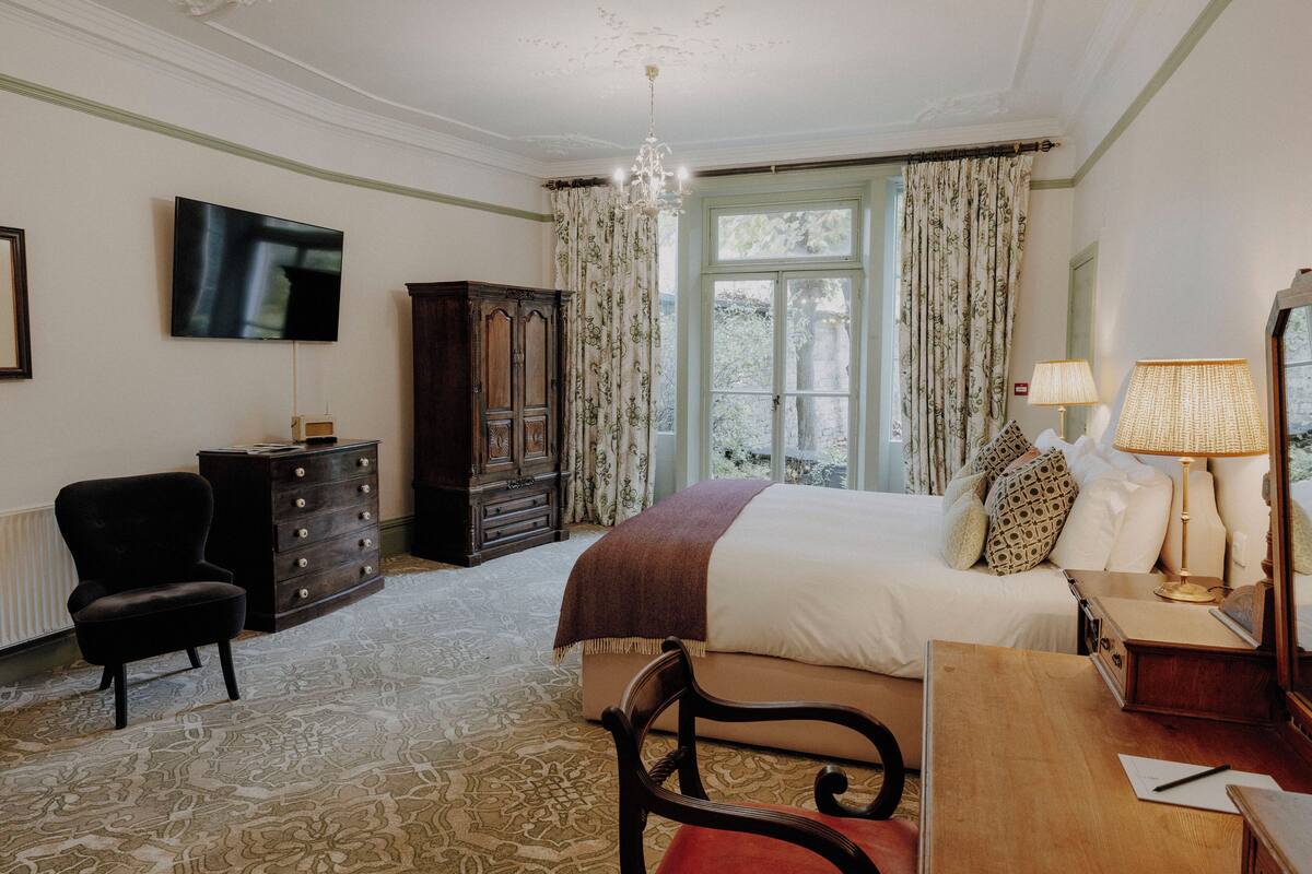 A bedroom with a bed, a desk, a chair, a dresser, a television, and a window with curtains.