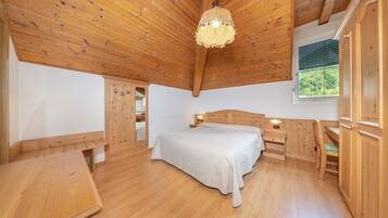 Ein Schlafzimmer aus Holz mit einem Bett, Nachttischen, einem Schreibtisch und einem Fenster.