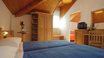 A bedroom with two beds, wooden furniture, a television, and a window.