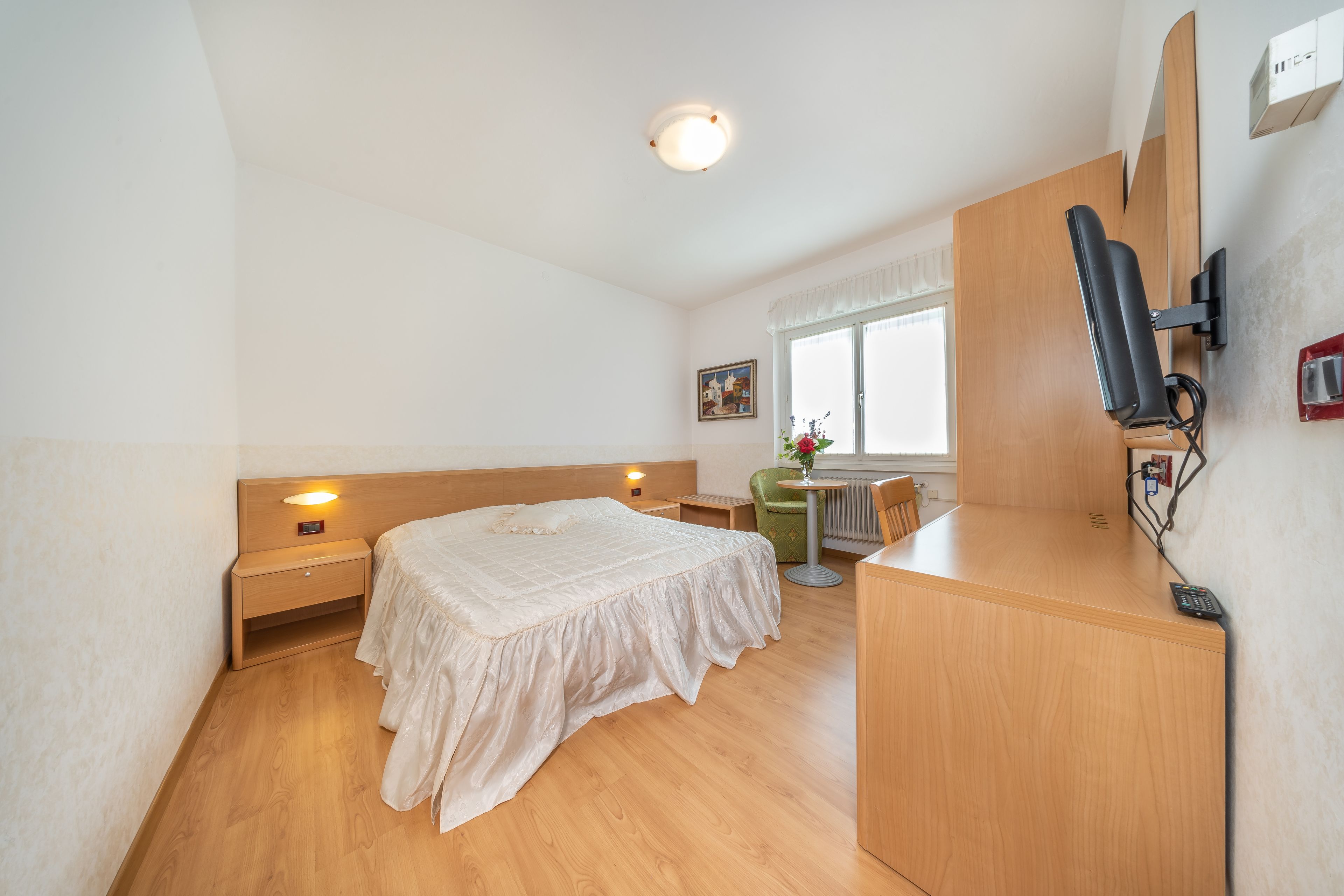 A bedroom with a bed, bedside tables, a desk, a chair, a radiator, and a window with curtains.