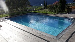 Una piscina rectangular con agua cristalina y azul, rodeada por una terraza de baldosas.