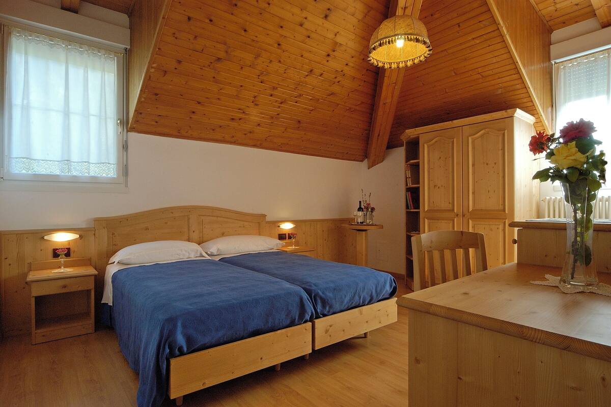A wooden bedroom with a double bed, bedside tables, a desk, and a chair.