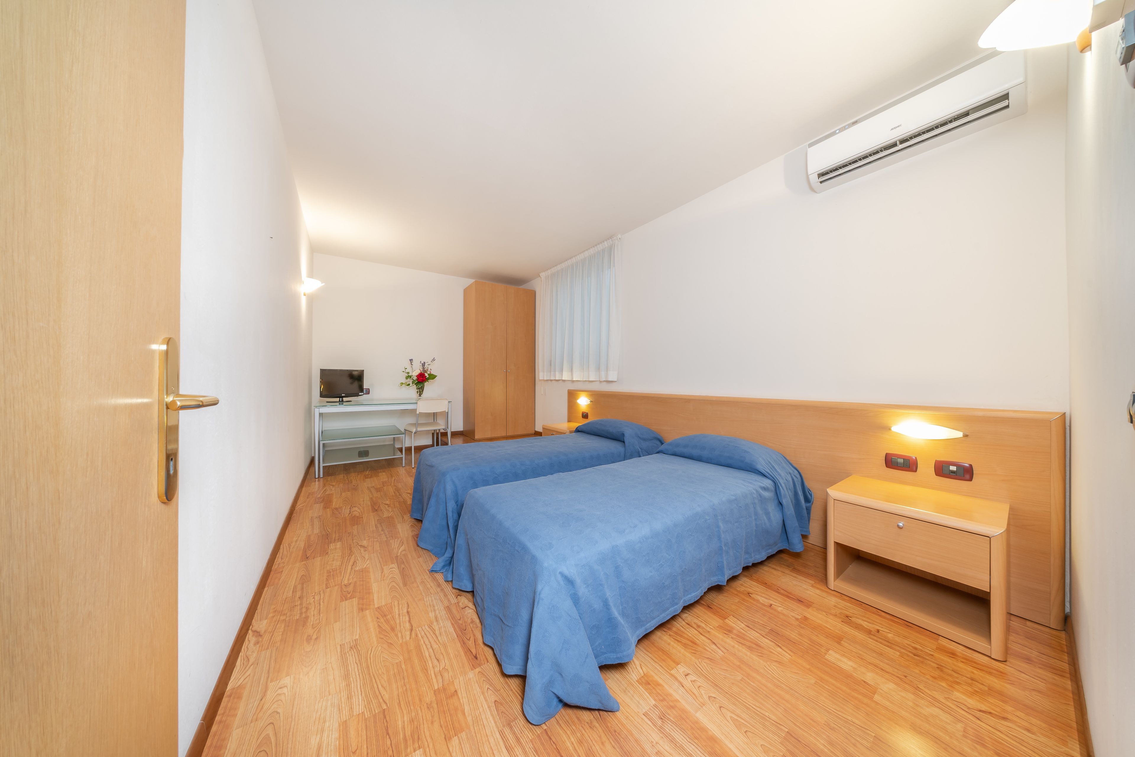 Una habitación de hotel con dos camas, un escritorio y una mesita de noche con lámpara.